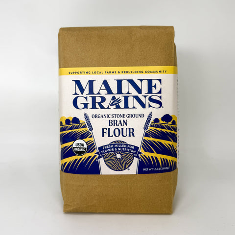 A bag of Maine Grains Organic Stone Ground Bran Flour, in a brown kraft paper bag with a white, blue, and yellow label, photographed on a clean white background.