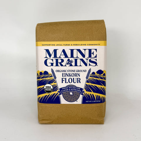 A 2 lb bag of Maine Grains Organic Stone Ground Einkorn Flour, featuring a kraft paper bag with a white, blue, and yellow label.