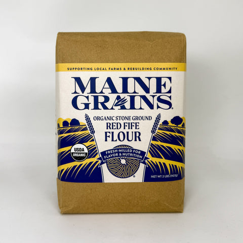 A package of Maine Grains Organic Stone Ground Red Fife Flour, featuring a brown kraft paper bag with a white and blue label.