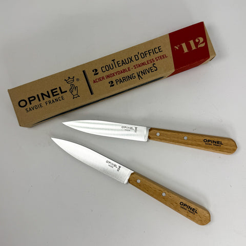 Two Opinel office knives with light brown wooden handles and silver stainless steel blades, displayed next to their original brown cardboard packaging box on a light gray background.