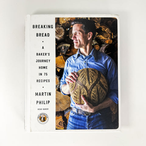 The book cover of 'Breaking Bread: A Baker's Journey Home in 75 Recipes' by Martin Philip, featuring a photo of a man holding a loaf of bread on a white background.