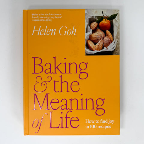 The front cover of the book 'Baking & the Meaning of Life' by Helen Goh, featuring a bright orange background with purple title text and a small food photograph in the top right corner, shown against a plain light background.