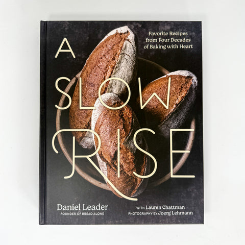 The book cover of 'A Slow Rise' by Daniel Leader, featuring a dark textured background with a photo of rustic sourdough bread in a bowl and large gold lettering, photographed on a light gray background.