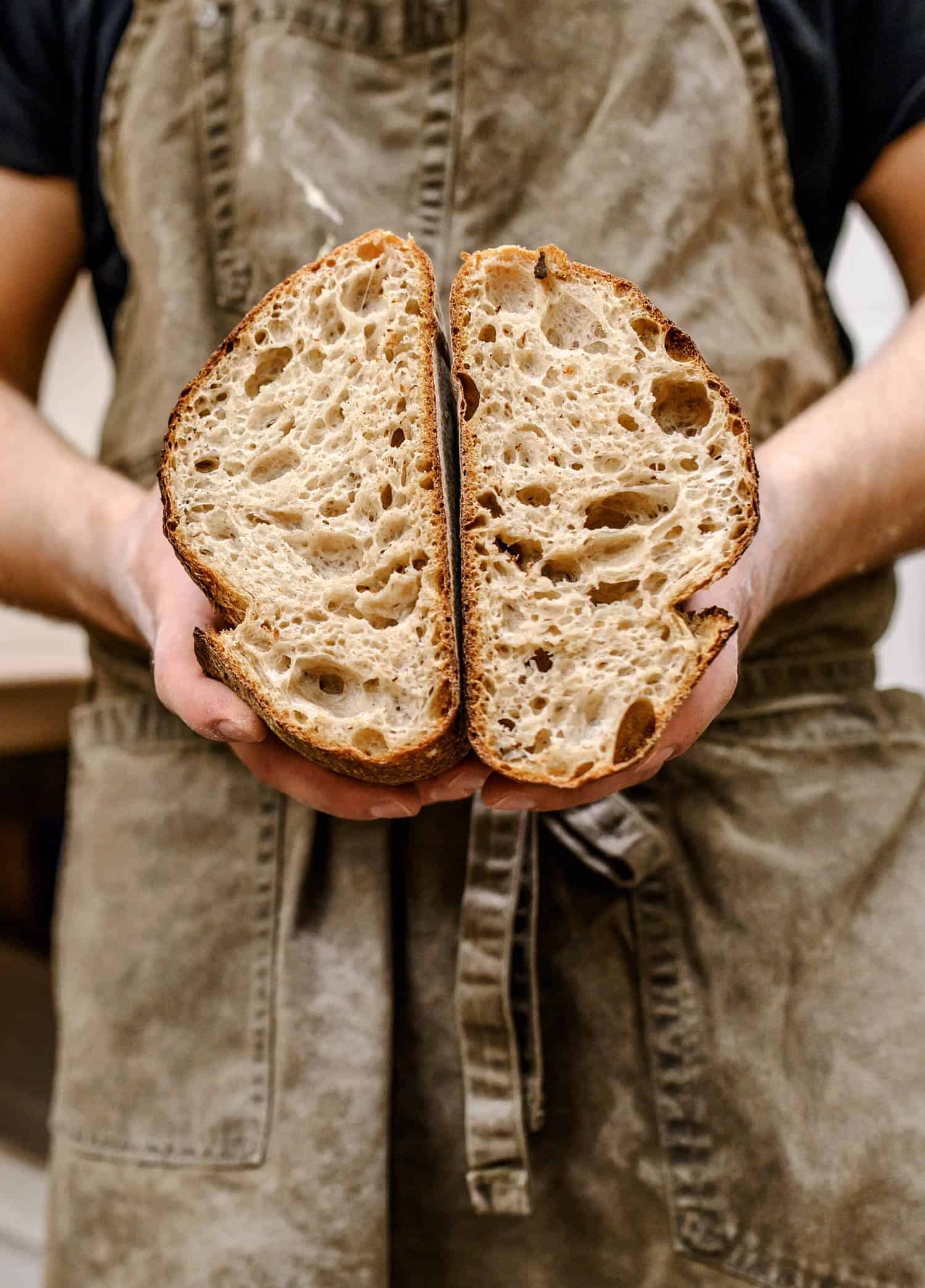 Baker holding a bread loaf cut open to reveal bubbles on the inside